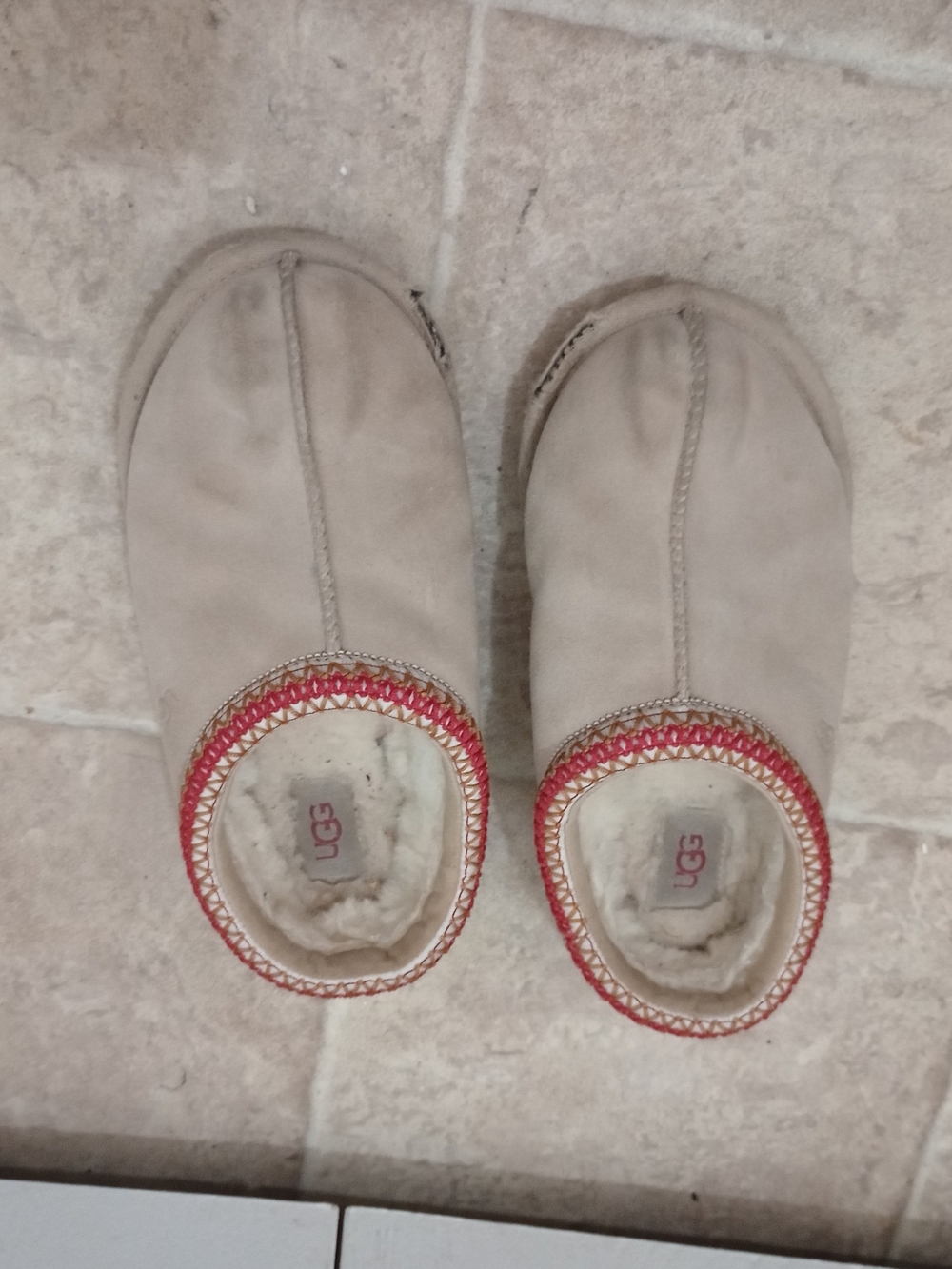 UGG Women's Tasman II slippers in a sand or beige color with red-patterned trim.